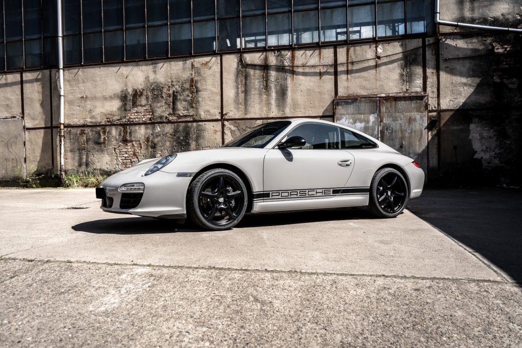 Porsche in der Farbe Chalk Grey mit alter Fabrikhalle im Hintergrund